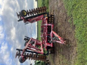 A disk tiller stored at the edge of a field. The arms of the tiller are vertical. 